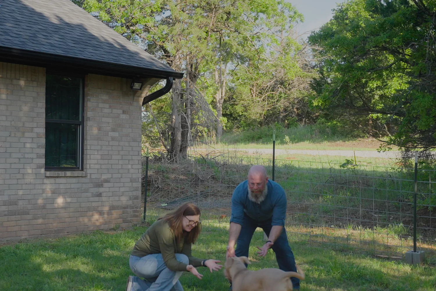 John e Ashley Hassell com seu cachorro no quintal de sua casa rural em Oklahoma, com uma Starlink no telhado.